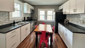 A modern kitchen with white cabinets, a wooden table, and red chairs.
