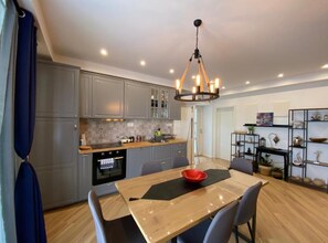 A modern kitchen with grey cabinets, a wooden dining table, and a chandelier. - Three Bedroom Apartment with Balcony (Dubrovnik)
