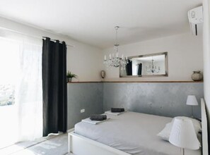 A bedroom with a bed, a chandelier, a mirror, and a window with curtains. - Three Bedroom Apartment with Balcony (Dubrovnik)