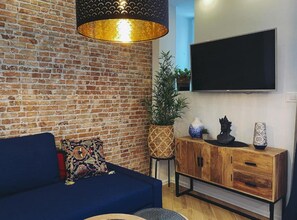 Un salon avec un mur en briques, un canapé bleu, un meuble en bois, une plante en pot et un téléviseur à écran plat.