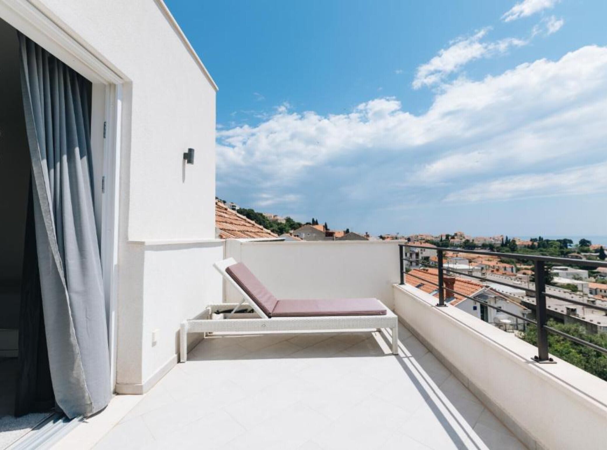 Uma varanda com chão branco, uma única poltrona de descanso e vista para a paisagem urbana.