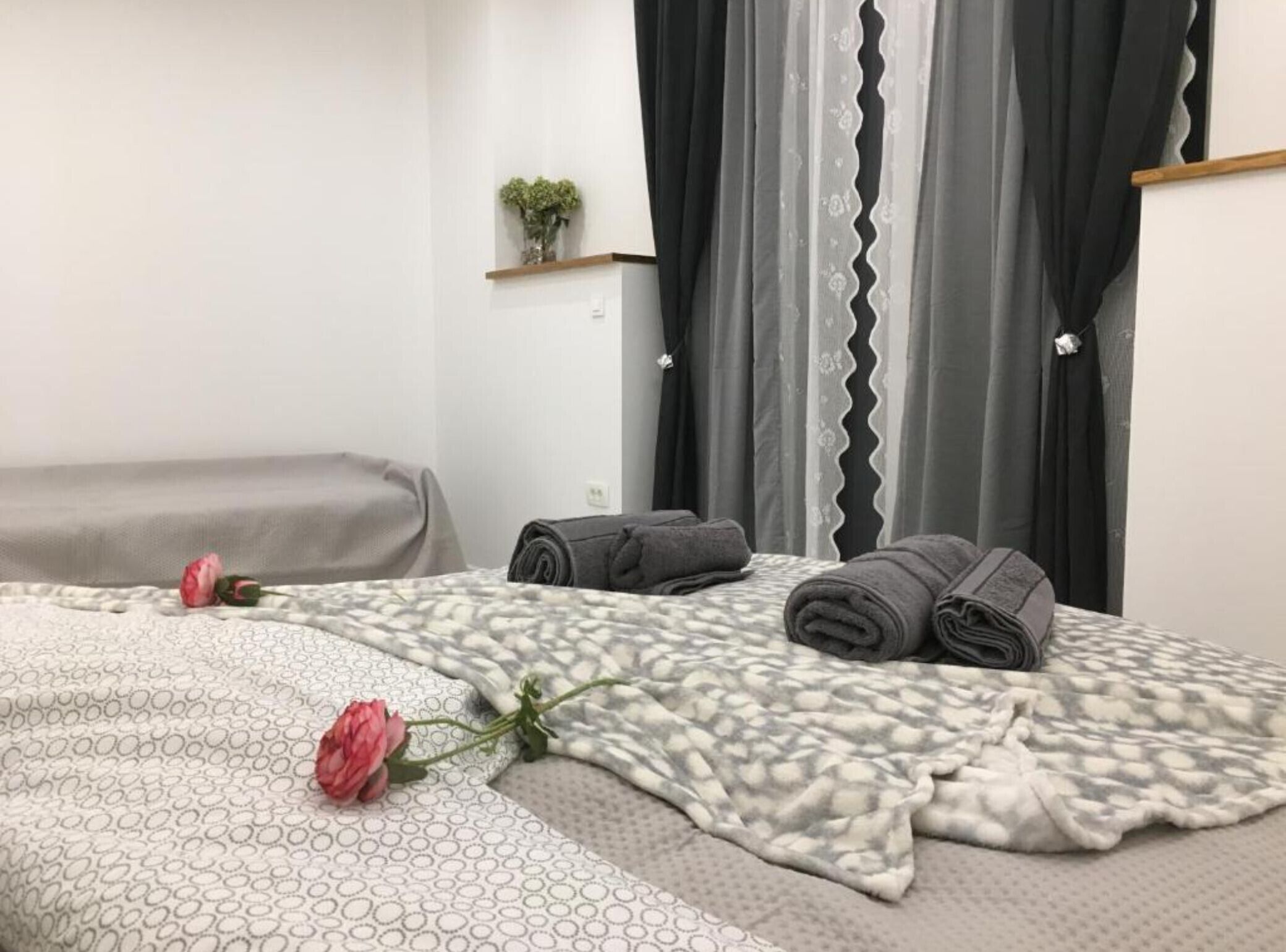 A neatly made bed with a patterned bedspread, two rolled-up towels, and a single rose on the bed.