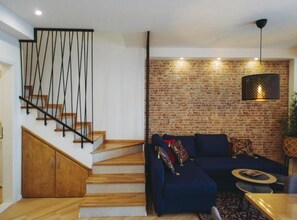 A modern living room with a wooden staircase, a brick wall, and a blue sofa set. - Three Bedroom Apartment with Balcony (Dubrovnik)