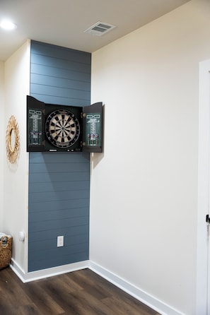 Ein Zimmer mit einem an einer blauen Wand befestigten Dartboard, einer weißen Tür und einem Holzboden.