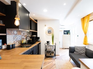 A modern kitchen with a wooden countertop, black cabinets, and a coffee machine. There is a dining area with a black sofa and a small table. - Marghareta Apartment NO 1 - TOP Location - Studio Apartment (Dubrovnik)