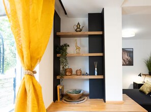 A room with a wooden floor, a black shelving unit with decorative items, a yellow curtain, and a view of the outdoors. - Marghareta Apartment NO 1 - TOP Location - Studio Apartment (Dubrovnik)