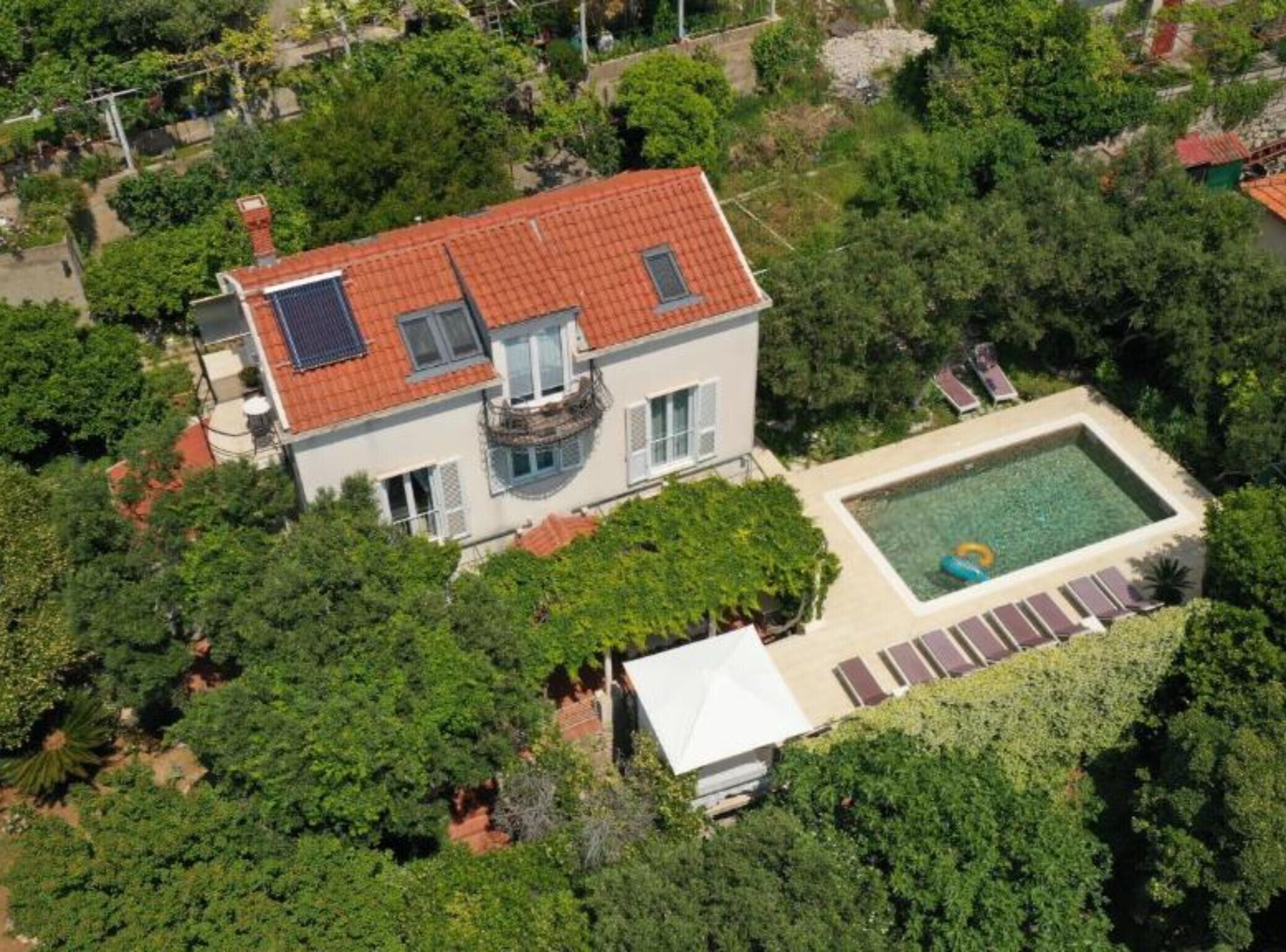 A two-story house with a red-tiled roof, a swimming pool, and a covered patio area.
