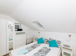 Een slaapkamer met een bed, een witte kledingkast, een bureau en een klein tafeltje.