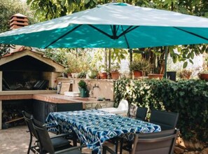 Een terras buiten met een tafel, stoelen en een barbecue.