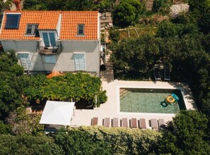 A two-story building with a tiled roof, a swimming pool, and a covered patio area. - Two Bedroom Apartment with Sea View and Balcony (Dubrovnik)