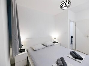 A modern bedroom with a bed, bedside tables, a mirror, and a door. - Two Bedroom Apartment with Sea View (Dubrovnik)