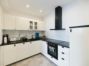 A modern kitchen with white cabinets, a black countertop, and a built-in oven. - Two Bedroom Apartment with Sea View (Dubrovnik)