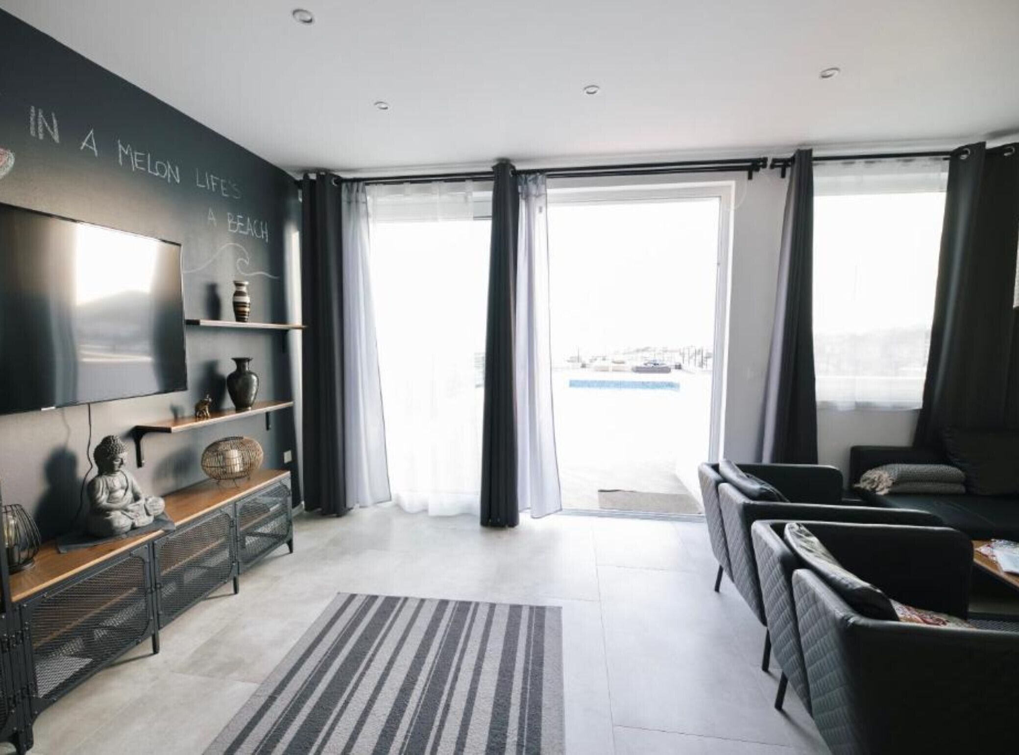 Een moderne woonkamer met een flatscreen televisie, een bank, een salontafel en een groot raam met gordijnen.