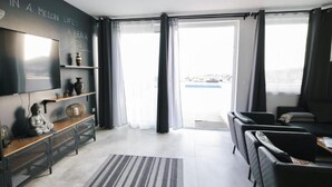 Ein modernes Wohnzimmer mit Flachbildfernseher, einer Couch, einem Couchtisch und einem großen Fenster mit Vorhängen.