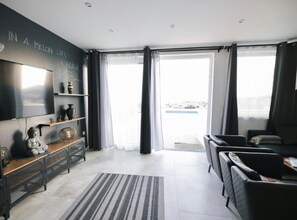 A modern living room with a flat-screen TV, a sofa, a coffee table, and a large window with curtains. - Two Bedroom Apartment with Sea View (Dubrovnik)