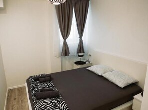 A bedroom with a bed, pillows, a bedside table, and curtains. - Two Bedroom Apartment with Sea View (Dubrovnik)
