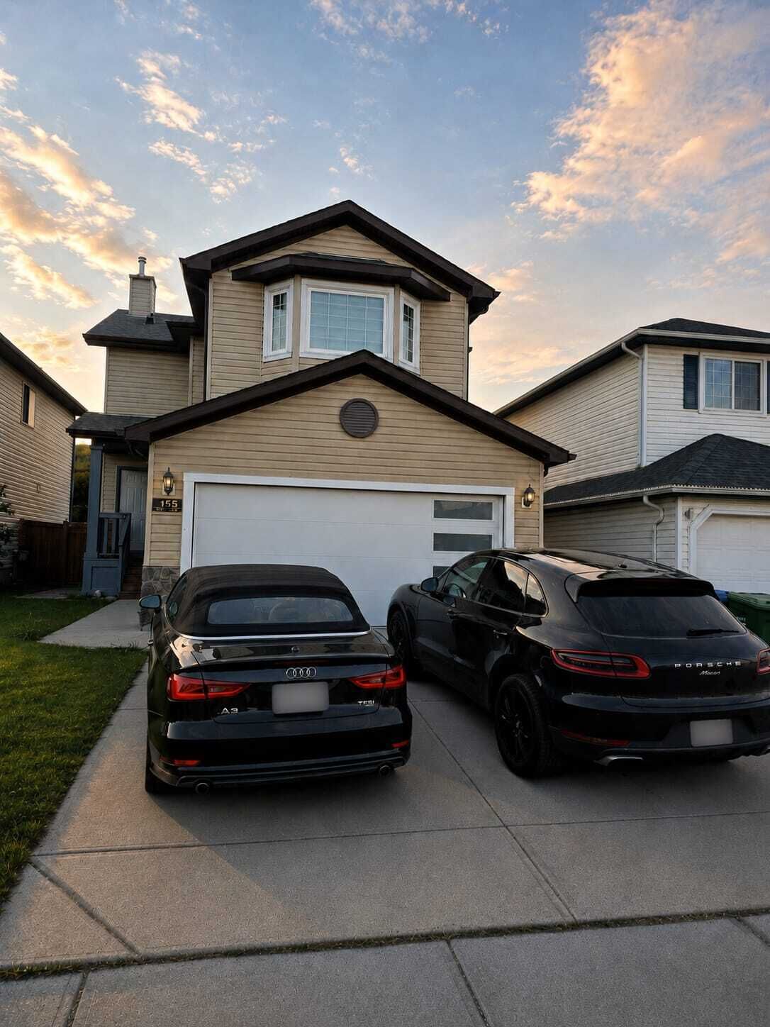 A two-story house with a garage, two parked cars, and a clear sky.