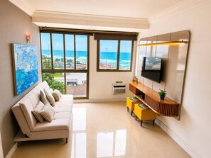 Ein Wohnzimmer mit einer Couch, einem Fernseher und einem großen Fenster mit Blick auf den Strand.