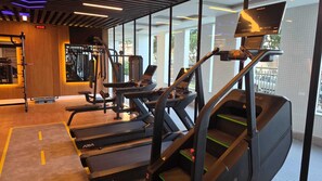 Een sportschool met loopbanden, krachtapparaten en een digitaal scherm.