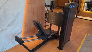 Ein Rudergerät in einem Fitnessraum mit Holzboden und Trainingsgeräten im Hintergrund.