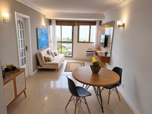 Ein modernes Wohnzimmer mit einer Couch, einem Esstisch mit Stühlen, einem an der Wand befestigten Fernseher und einem großen Fenster mit Blick.