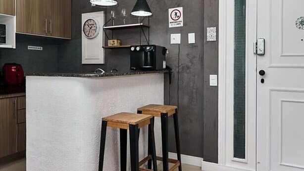 Cuina amb una illa central, dos tamborets de bar, il·luminació penjant i una porta amb panell de vidre opac.