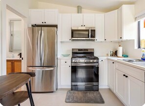 A compact kitchen with white cabinets, a stainless steel refrigerator, a microwave, and a stove. - Newly Built Modern Guest House • Cozy w/ Kitchen (Los Angeles)