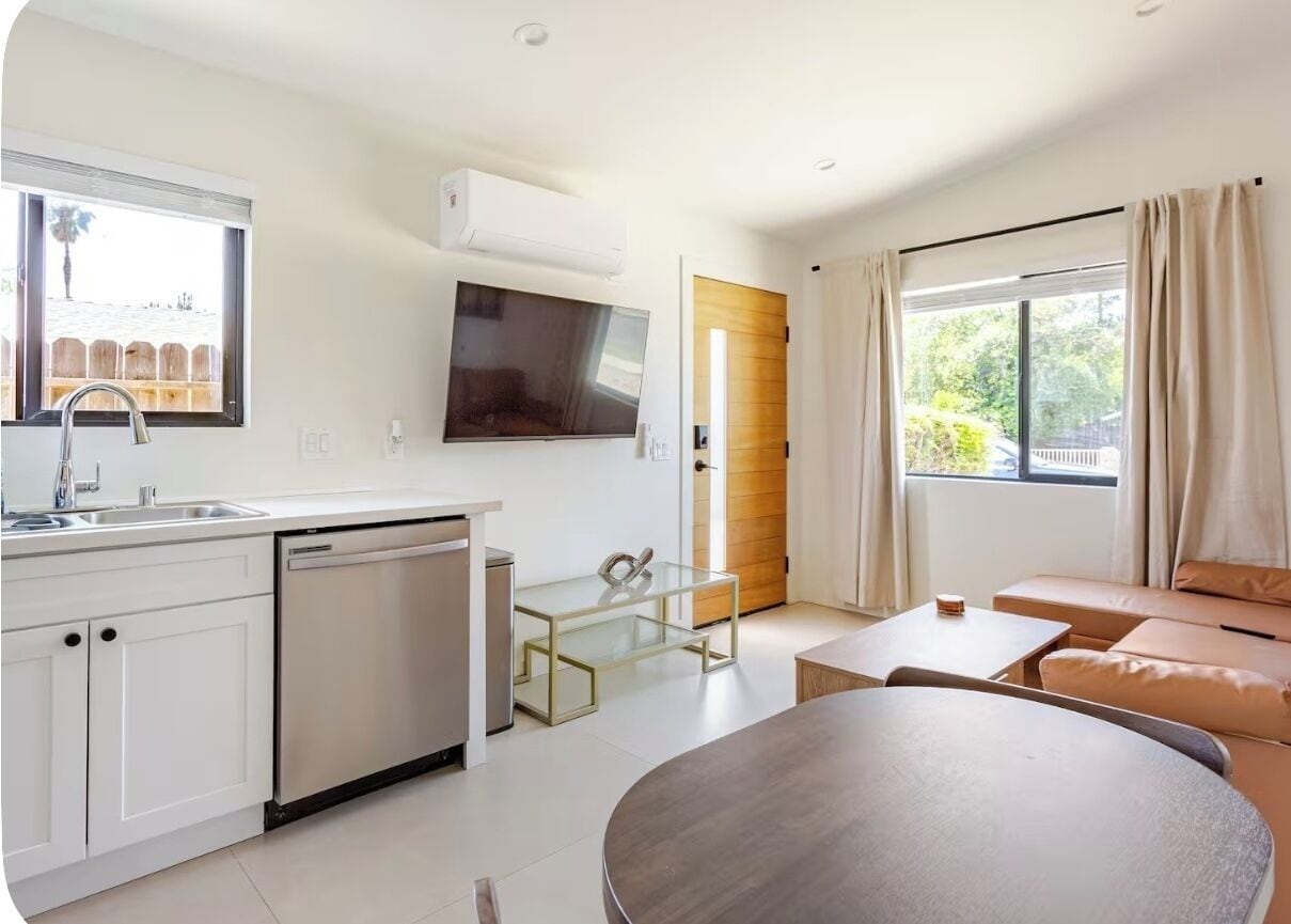 A modern kitchen with a dishwasher, a glass table, and a large window.