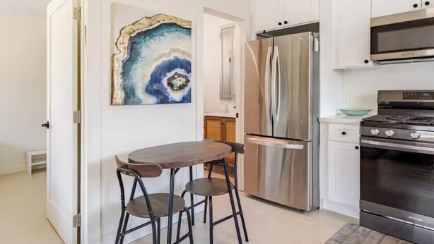 A modern kitchen with white cabinets, a stainless steel refrigerator, a Samsung oven, and a dining area with a table and stools. - Newly Built Modern Guest House • Cozy w/ Kitchen (Los Angeles)