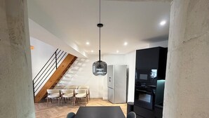 Een moderne keuken met een zwart aanrecht, roestvrijstalen apparatuur en een houten eettafel met stoelen.