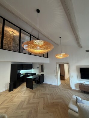 A spacious living area with a high ceiling, a kitchen with modern appliances, and a dining area with a herringbone wood floor. - Luxury Apartment in the Heart of the Alpilles (Saint-Rémy-de-Provence)