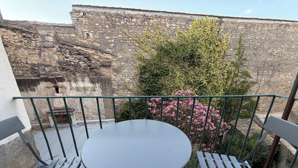 Een balkon met een ronde tafel en bankjes, met uitzicht op een stenen muur en groen.