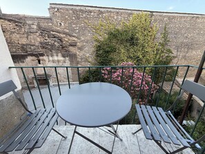 A balcony with a round table and benches, overlooking a stone wall and greenery. - Luxury Apartment in the Heart of the Alpilles (Saint-Rémy-de-Provence)