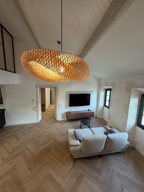 A spacious living area with a herringbone wood floor, a large sofa, a TV, and a unique woven pendant light. - Luxury Apartment in the Heart of the Alpilles (Saint-Rémy-de-Provence)