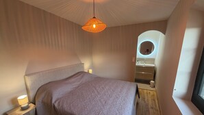 Een slaapkamer met een groot bed, bedlampjes, een hanglamp, een ingebouwde ronde spiegel en een raam.