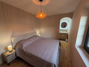 Ein Schlafzimmer mit einem großen Bett, Nachttischlampen, einer Pendelleuchte, einem eingelassenen runden Spiegel und einem Fenster.