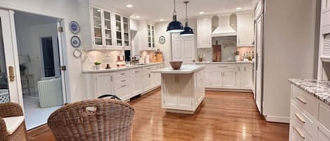 A spacious kitchen with white cabinetry, a central island, and a hanging pendant light.