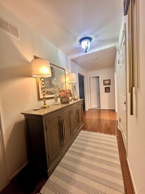 A hallway with a dark wooden console, two wall-mounted lamps, a mirror, and a ceiling light fixture. - Normandy H. a charming house in silver spring. 5 min from The Adventist Hospital (Silver Spring)