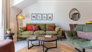A modern living room with a green sofa, two round coffee tables, a floor lamp, and framed artwork on the wall. - Neo-African apartment at the entrance of Durbanville wine route (Cape Town)