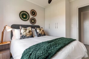 A bedroom with a bed, a nightstand, a lamp, and wall decorations. - Neo-African apartment at the entrance of Durbanville wine route (Cape Town)