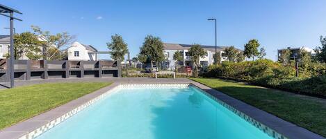 A swimming pool with a tiled edge, surrounded by a grassy area and residential buildings.
