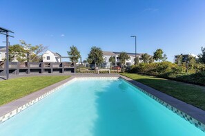 A swimming pool with a tiled edge, surrounded by a grassy area and residential buildings. - Neo-African apartment at the entrance of Durbanville wine route (Cape Town)