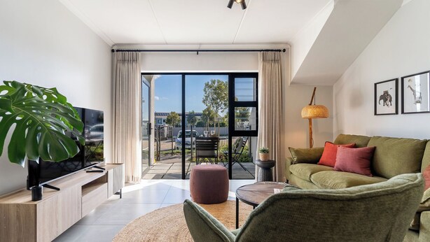 A modern living room with a flat-screen TV, a green sofa, a coffee table, and a large plant. - Neo-African apartment at the entrance of Durbanville wine route (Cape Town)