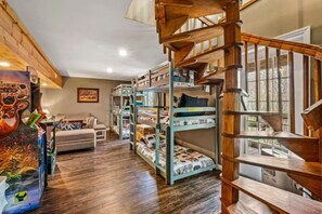 A bunk bed room with a wooden staircase and a sofa. - Smoky Bear Chalet | Hot Tub & Gazebo | Sleeps 12 (Gatlinburg)