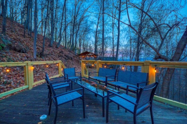 Una terrazza esterna con tavolo e sedie in vetro, circondata da una ringhiera in legno con luci a stringa.