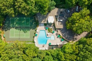 Vista aerea di una proprietà con campo da tennis, piscina e area parcheggio, circondata da alberi.