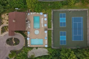 An aerial view of a property with a swimming pool, tennis courts, and a building with a red roof. - Smoky Bear Chalet | Hot Tub & Gazebo | Sleeps 12 (Gatlinburg)