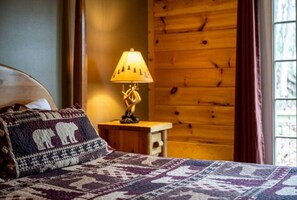 Ein Bett mit einem gemusterten Überwurf, ein Nachttisch mit einer Lampe und eine Holzwand.