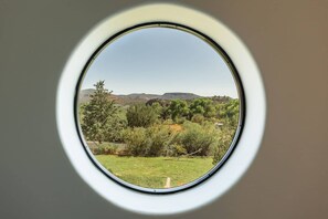 Ein rundes Fenster mit Blick auf eine grüne Landschaft, Bäume und ferne Hügel.