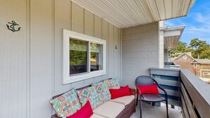 Un balcon avec un canapé et une chaise en osier, une fenêtre et un mur en briques.